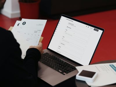 Persona salīdzina papīra rēķinu ar portatīvā datora ekrānā atvērtu programmu.