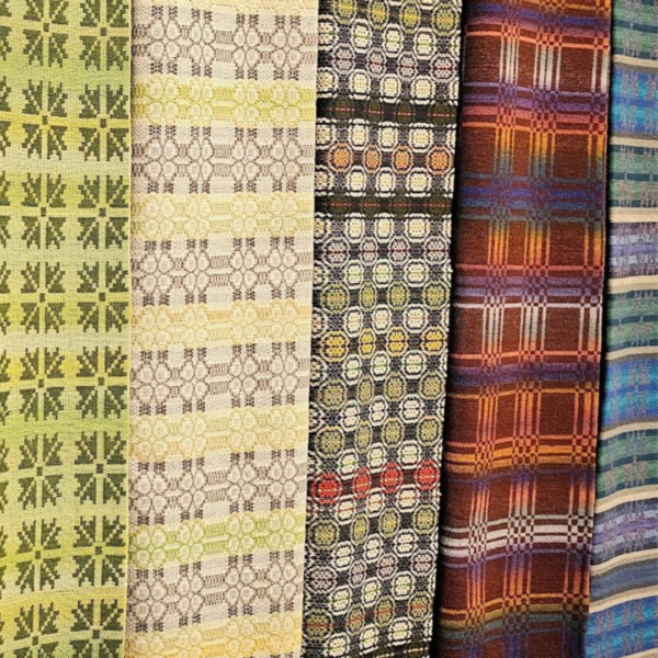 Vertikāli izvietoti pieci austu audumu paraugi ar atšķirīgiem rakstiem: gaiši zaļš ar stilizētām zvaigznēm, bēšs ar smalkiem savienotiem aplīšiem, tumšs ar krāsainiem ģeometriskiem astoņstūriem, brūns rūtains un zili-zaļš svītrains.