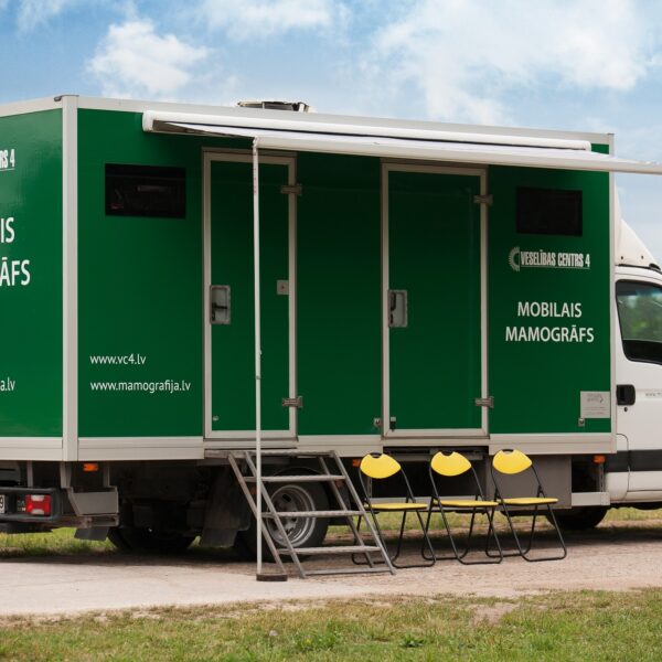 Zaļi-balts kravas auto ar numura zīmi HK-349, uz kura sāniem rakstīts "VESELĪBAS CENTRS 4" un "MOBILAIS MAMOGRĀFS", kā arī "www.vc4.lv" un "www.mamografija.lv", stāv ārā ar izvilktu nojumi, kāpnēm un trim dzelteniem saliekamiem krēsliem.